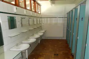Helle Sanitäranlage mit mehreren Waschbecken, Spiegeln und grünen Türen, gefliestem Boden und langen Flurwänden.