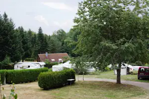 Wohnwagen und Wohnmobil auf einem Campingplatz zwischen Hecken und Bäumen, mit gepflastertem Weg und Rasenfläche.