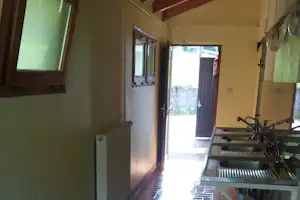 Innenansicht eines Campinghauses mit offener Tür zur Terrasse, Holzwand, Fenster und Bank am Eingang.