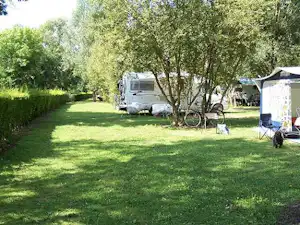 Wohnwagen und Zelt auf einem grünen Campingplatz zwischen Bäumen, mit Fahrrad und Gartenmöbeln am Stellplatz.