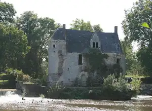 Altes Schlossgebäude am Fluss, umgeben von Bäumen und Grün, mit Wasserlauf im Vordergrund.