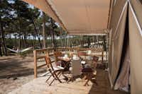 Camping La Grigne  -  Mobilheim vom Campingplatz mit gedecktem Esstisch auf der Veranda, Kind in Hängematte im Hintergrund