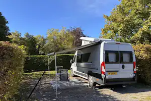 Wohnmobil auf einem Stellplatz mit Vorzelt, befestigtem Weg und Bäumen im Hintergrund.