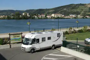 Wohnmobil auf dem Campingplatz am See, Blick auf Wasser, Uferpromenade und Hügel mit Häusern im Hintergrund.