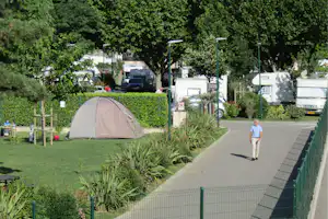 Zelt auf dem Campingplatz, daneben Wohnmobile und ein Mann auf dem Weg, umgeben von Bäumen und Hecken.
