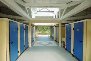 Blaue Schließfächer in einem überdachten Flur eines Campinggebäudes, mit hellen Wänden und Bodenfliesen.