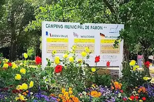 Blumenbeet mit bunten Blüten vor einem Campingplatz-Schild und Infotafel im Grünen, umgeben von Bäumen.
