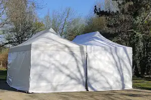 Zwei weiße Campingzelte auf einem grasigen Platz, davor eine Holzbank und ein Weg zwischen Bäumen.