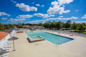 Schwimmbecken mit Liegestühlen und Sonnenschirmen auf dem Terrassenbereich, im Hintergrund Bungalows und Bäume.
