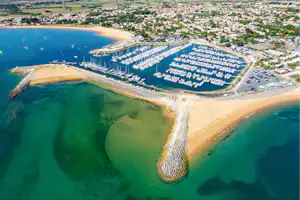 Luftaufnahme von Hafenanlagen mit vielen Booten, Stegen und einem Sandstrand an der Küste.