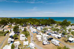 Campingplatz mit Wohnmobilen und Stellplätzen, Bäumen und Wegen, Blick auf das Meer und den blauen Himmel.
