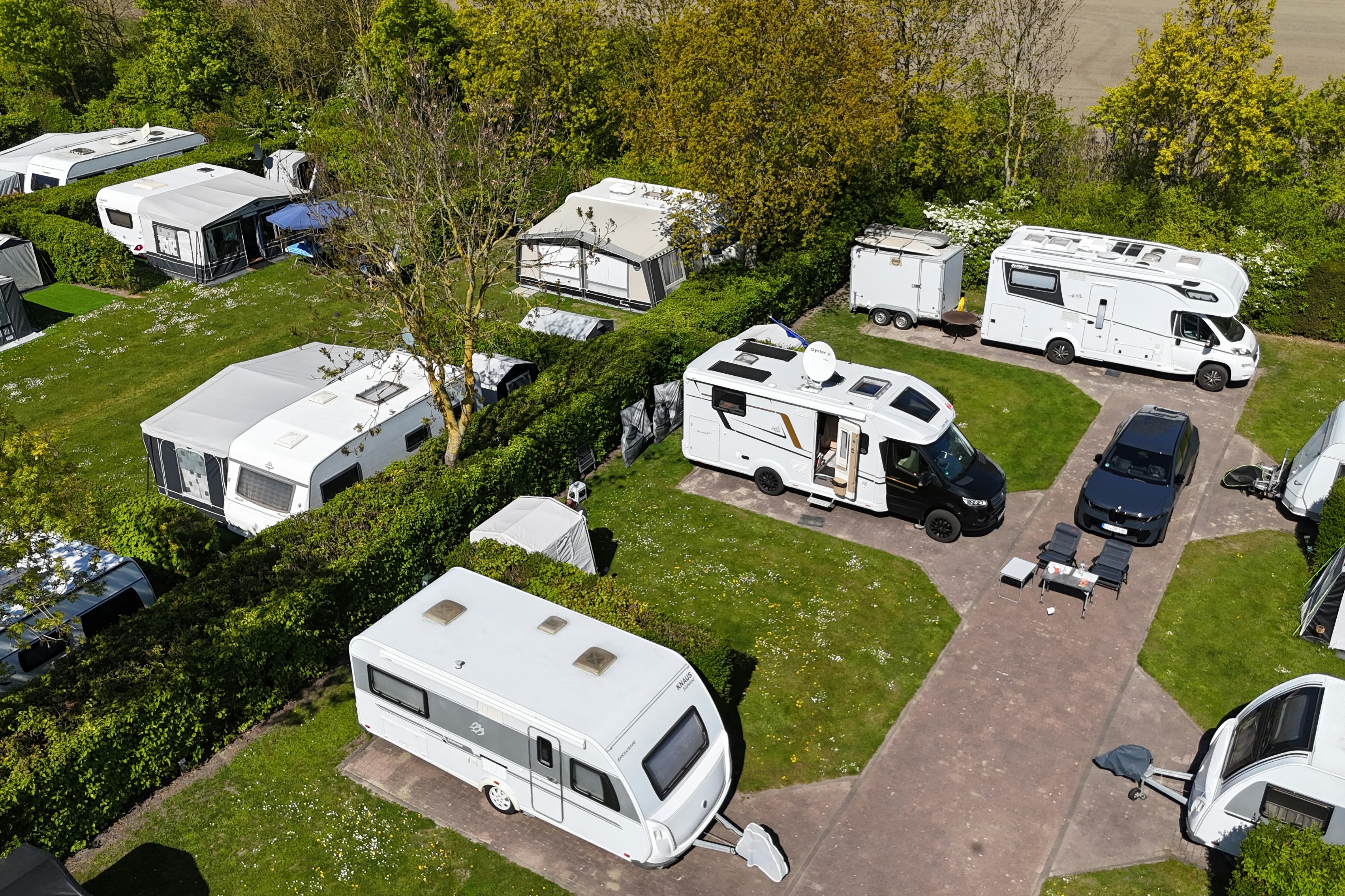 Wohnmobile und Caravans auf einem Campingplatz mit Rasenflächen, Wegen und Bäumen im Hintergrund.