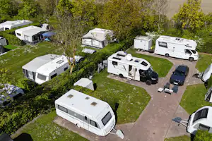 Wohnmobile und Caravans auf einem Campingplatz mit Rasenflächen, Wegen und Bäumen im Hintergrund.