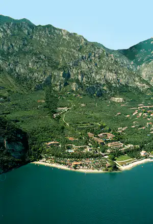 Campinganlage am See mit Strand, umgeben von grünen Bergen und vielen Gebäuden im Tal.