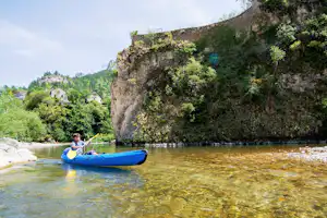 Blaues Schlauchboot auf klarem Flusswasser, im Hintergrund grüne Hänge und ein kleines Gebäude am Ufer.