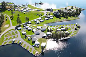 Campingplatz am See mit vielen Stellplätzen und Wohnwagen, umgeben von Grün und Bäumen, Blick von oben auf das Ufer.