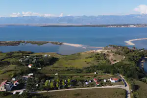 Blick von oben auf einen Campingplatz am Meer mit Wohnwagen, Wegen und Grünflächen, im Hintergrund Berge und Küste.