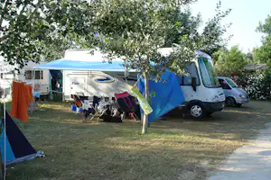 Wohnmobil und Zelte auf einem Campingplatz unter einem Baum, mit Campingstühlen und Tisch im Vordergrund.