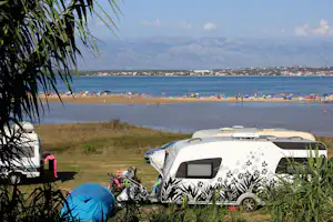 Wohnwagen und Zelt am Campingplatz mit Blick auf den Strand, das Meer und eine Küstenstadt in der Ferne.