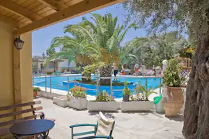 Blick von der Terrasse auf den Camping-Pool mit Palmen, Sitzgelegenheiten und Blumenbeeten neben dem Wasser.