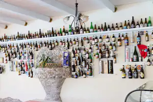 Barbereich mit Wand voller Flaschen, Steinwand und Beleuchtung, daneben Fenster und Deko im Innenraum.