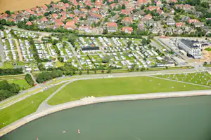 Luftaufnahme eines Campingplatzes am See mit vielen Stellplätzen, Wohnmobilen, Bäumen, Wegen und einem großen Gebäude am Ufer.