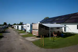 Wohnmobil auf einem Stellplatz mit Sonnensegel, daneben weitere Wohnmobile und ein gepflasterter Weg am Campingplatz.