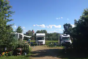 Wohnmobile auf einem Campingplatz im Grünen, Kiesweg zwischen Stellplätzen, Bäume und Wiese im Hintergrund.