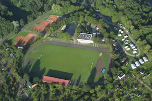 Luftaufnahme einer Campinganlage mit großen Rasenflächen, Wegen, mehreren Stellplätzen und Gebäuden im Grünen.