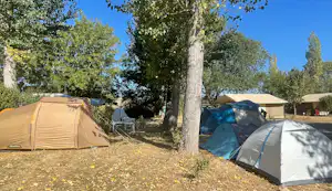 Zwei Campingzelte am Waldrand unter hohen Bäumen, mit kleinem Tisch und Stühlen am Zeltplatz.
