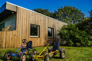 Holzhaus am Campingplatz mit zwei gelben und blauen Quads auf dem Rasen vor den Fenstern.