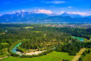Fluss schlängelt sich durch ein grünes Tal mit Wald und Wiesen, im Hintergrund Berge und ein weiter Himmel.