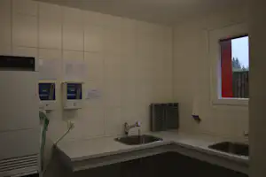 Camping-Badezimmer mit zwei Waschbecken, Fliesenwand, Spendern und Fensteröffnung mit Blick nach draußen.