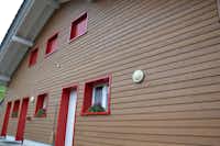 Camping Oberiberg - Ferienwohnungen mit roten Fenstern und Holzfassade 