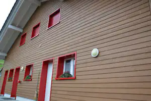 Holzfassade eines Ferienhauses mit roten Türen und Fenstern, daneben ein Vordach und ein Blumenkasten.