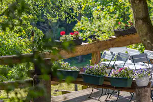 Terrasse am Campingplatz mit Gartenstühlen, Holzboden und Blumenkästen an einem Zaun im Grünen.