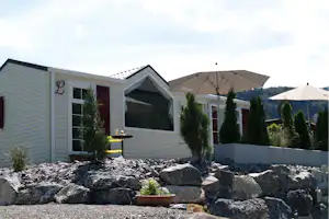 Campinghaus mit Markise und Sonnenschirmen, davor Kiesbeet mit Steinen und kleinen Bäumen vor dem Gebäude.