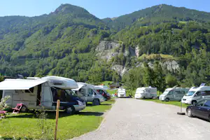 Wohnmobile auf einem Campingplatz am Hang, Blick auf grüne Berge und Felswand im Hintergrund.