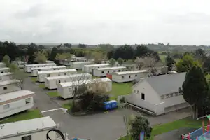 Blick auf eine Campinganlage mit mehreren Mobilheimen, Wegen und Rasenflächen, umgeben von Bäumen und grüner Landschaft.