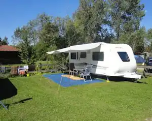Wohnwagen auf einem Campingplatz im Grünen mit Vorzelt, Campingstühlen und Sonnenschirm, umgeben von Bäumen.