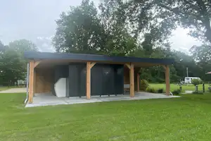 Moderner Stellplatz mit überdachtem Holzcarport und Vorzelt, daneben Rasen und Bäume im Campinggelände.