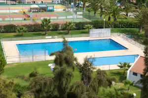 Blick auf zwei Camping-Pools mit blauem Wasser, Palmen und gepflegtem Rasen, im Hintergrund Tennisplätze und Gebäude.