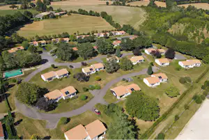 Luftaufnahme eines Campingplatzes mit mehreren Stellplätzen, Wohnwagen und Wegen, umgeben von Wiesen und Bäumen.