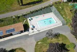 Luftaufnahme eines Campingplatzes mit großem Schwimmbecken, Liegen am Beckenrand und Wegen zwischen Rasenflächen.