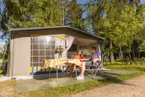 Camping Olympia - Camperpaar vor ihrem Wohnwagen in der Sonne