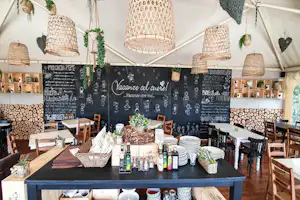 Innenansicht eines Campingzelts mit Bar-Tisch, Holzstühlen, Regalen mit Flaschen und einer Tafel mit handschriftlichen Texten.
