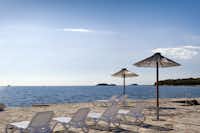 Camping Orsera  -  Sonnenschirme und Liegestühle vom Campingplatz mit direktem Zugang zum Meer