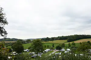 Campingplatz im Tal mit Wohnwagen und Zelten, Blick auf Wiesen und Bäume in der Landschaft.