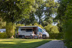 Wohnmobil mit Markise auf dem Campingplatz, zwei Personen sitzen am Tisch vor dem Fahrzeug im Grünen.