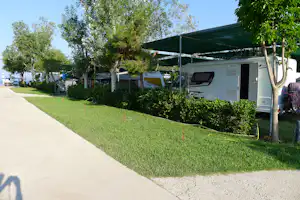 Wohnwagen mit Vorzelt auf einem Campingplatz, daneben Rasenfläche, Hecken und ein gepflasterter Weg.